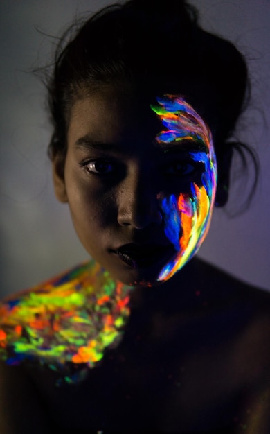 Portrait en gros plan d'une jeune femme avec la peinture du visage dans la chambre noire