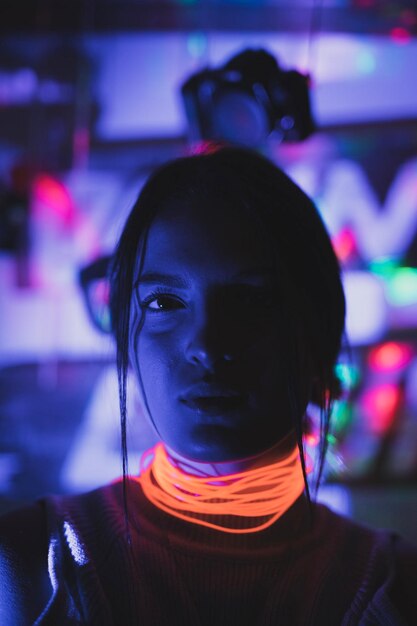 Photo portrait en gros plan d'une jeune femme sérieuse portant un collier illuminé dans une chambre noire la nuit