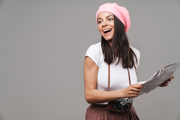 Portrait en gros plan d'une jeune femme touristique joyeuse avec un appareil photo vintage rétro se demandant et tenant une carte papier isolée sur un mur gris