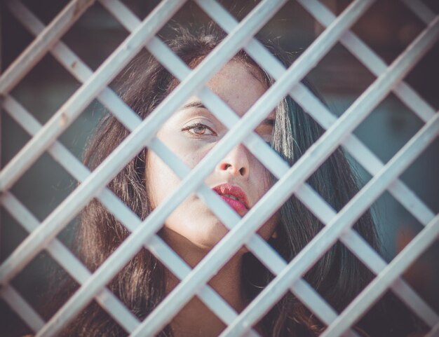Portrait en gros plan d'une jeune femme vue à travers une clôture métallique