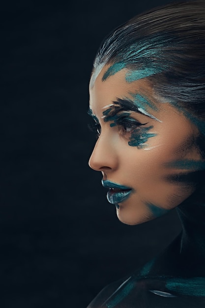 Portrait en gros plan d'une jeune fille de beauté avec un maquillage créatif. Des ombres bleues et noires peintes sur son visage. Idée conceptuelle.