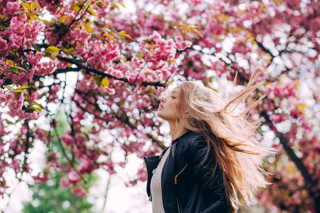 Un portrait en gros plan d'une jeune fille blonde dans le contexte d'un arbre à fleurs japonais de sakura. Une belle jeune femme aux longs cheveux blonds dans le parc du printemps.