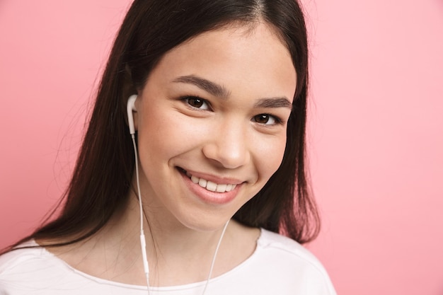 Portrait en gros plan d'une jeune fille séduisante portant des écouteurs regardant à l'avant avec un sourire isolé sur un mur rose