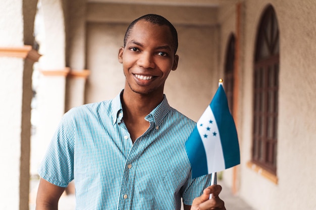 Portrait en gros plan d'un jeune homme d'ascendance africaine regardant la caméra tenant un petit drapeau du honduras