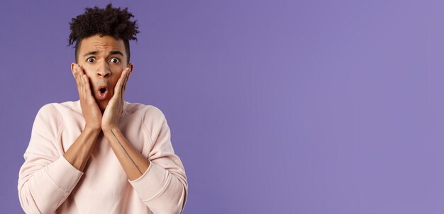 Portrait en gros plan d'un jeune homme embarrassé concerné, tenir les mains sur les joues, l'air désespéré et alarmé