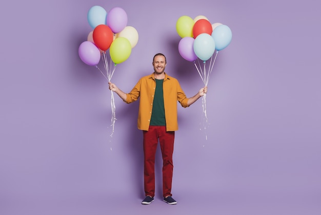 Photo portrait en gros plan d'un jeune homme joyeux, invité à la fête, tenir des ballons sur un mur violet