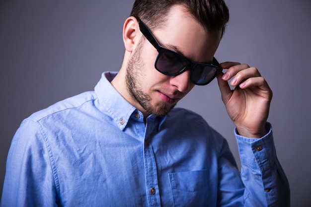 Portrait en gros plan d'un jeune homme à lunettes de soleil sur fond gris