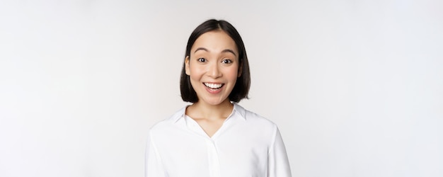 Portrait en gros plan d'une jeune mannequin asiatique qui a l'air étonnée de la caméra en souriant des dents blanches debout sur fond blanc