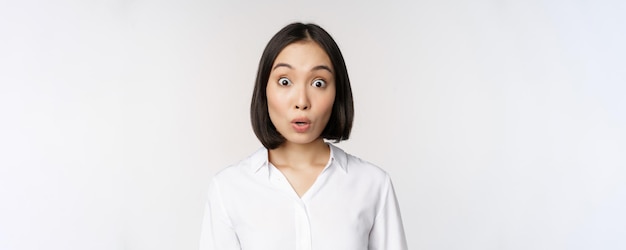 Portrait en gros plan d'une jeune mannequin asiatique qui a l'air étonnée de la caméra en souriant des dents blanches debout sur fond blanc