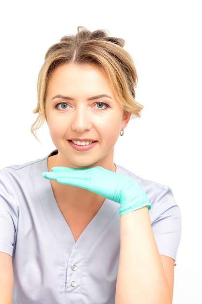 Portrait en gros plan d'une jeune travailleuse de la santé caucasienne souriante debout et regardant la caméra portant des gants sur fond blanc