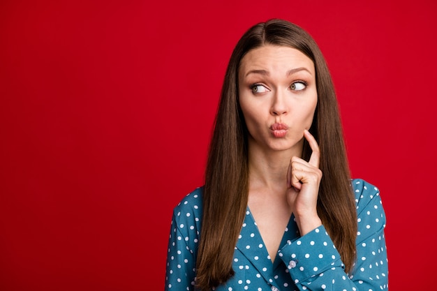 Portrait en gros plan d'une jolie fille aux cheveux bruns curieuse pensant à l'espace de copie lèvres moue isolées sur fond de couleur rouge vif