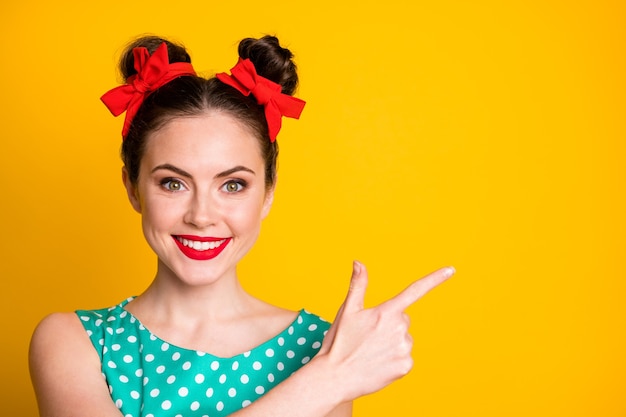 Portrait en gros plan d'une jolie fille joyeuse vêtue d'une robe bleu sarcelle en pointillé montrant un espace de copie isolé sur un fond de couleur jaune vif