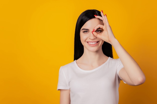 Portrait en gros plan d'une jolie fille montrant les doigts signe d'accord isolé sur fond de couleur jaune vif