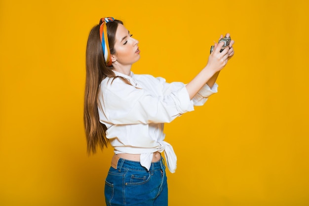 Portrait en gros plan d'une jolie fille souriante en robe prenant une photo sur un appareil photo rétro isolé