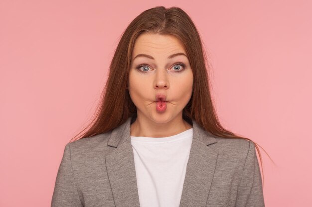 Photo portrait en gros plan d'une jolie jeune femme drôle en costume d'affaires faisant face à un poisson avec des lèvres boudeuses regardant avec une grimace maladroite humoristique étonnement comique prise de vue en studio intérieur isolé sur fond rose