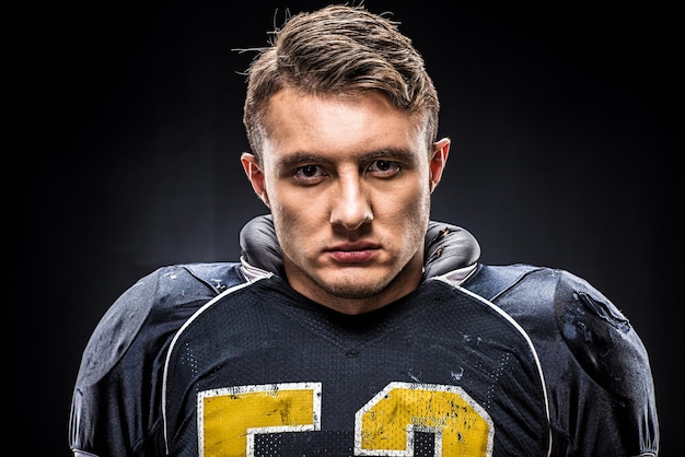 Portrait en gros plan d'un joueur de football américain en uniforme regardant la caméra sur le noir