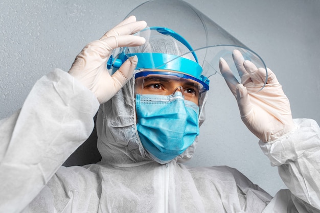 Portrait en gros plan d'un médecin portant une combinaison EPI contre le coronavirus et le covid-19, sur fond de mur gris.