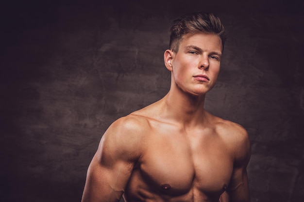 Portrait en gros plan d'un modèle sexy de jeune homme torse nu avec un corps musclé et une coupe de cheveux élégante posant dans un studio. Isolé sur un fond sombre.