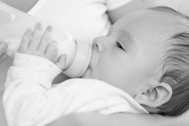 Portrait en gros plan noir et blanc d'un mignon petit garçon de 3 mois buvant du lait de la bouteille