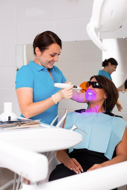 Portrait en gros plan d'une patiente chez le dentiste de la clinique Procédure de blanchiment des dents avec lampe UV à lumière ultraviolette