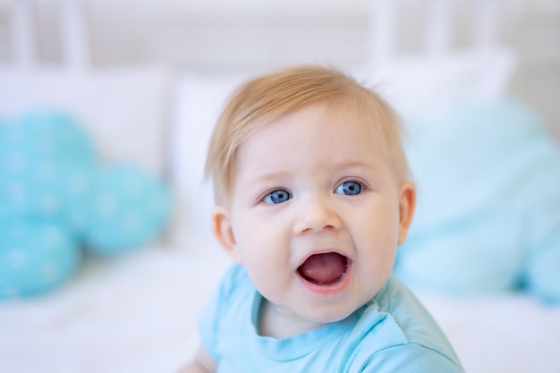 portrait en gros plan d'un petit bébé blond souriant bébé aux yeux bleus à la maison sur le lit