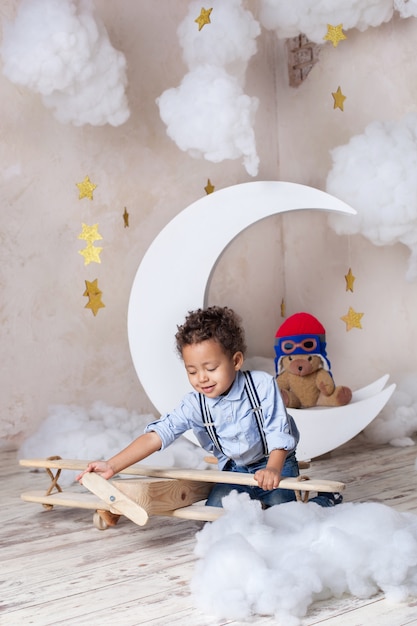 Portrait de gros plan d'un petit garçon afro-américain bouclé. Le garçon noir. école, éducation préscolaire. Rêve, carrière. Petit garçon joue avec un avion en bois jouet écologique à la maternelle. Enfance, imagination.