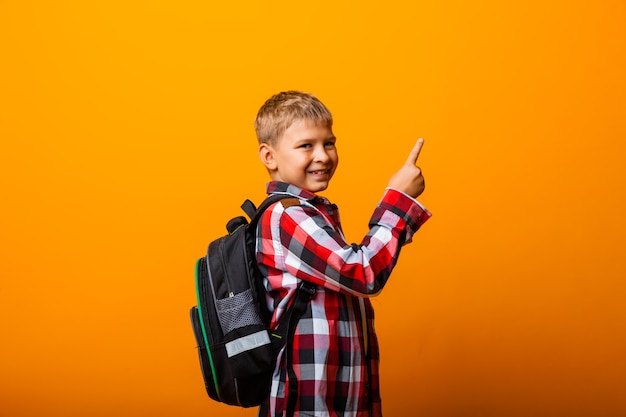 Portrait en gros plan d'un petit garçon étudiant joyeux pointant vers une excellente idée, sur fond jaune