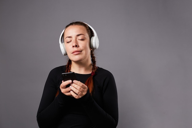 Portrait en gros plan d'un podcast féminin caucasien ou d'une écoute de musique sur fond gris. écouter de la musique au casque