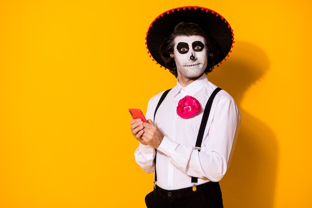 Portrait en gros plan de son beau beau mec effrayant gai drôle caballero utilisant l'application gadget de l'appareil 5g blogg calavera célébration du carnaval isolé brillant vif éclat vibrant fond de couleur jaune