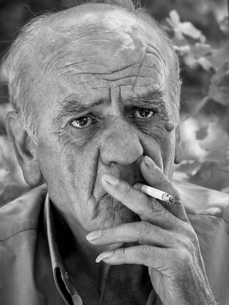 Portrait en gros plan d'un vieux retraité grec sérieux qui fume une cigarette en noir et blanc