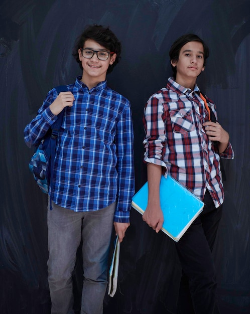 Portrait de groupe d'adolescents arabes contre un tableau noir portant un sac à dos et des livres dans une salle de classe