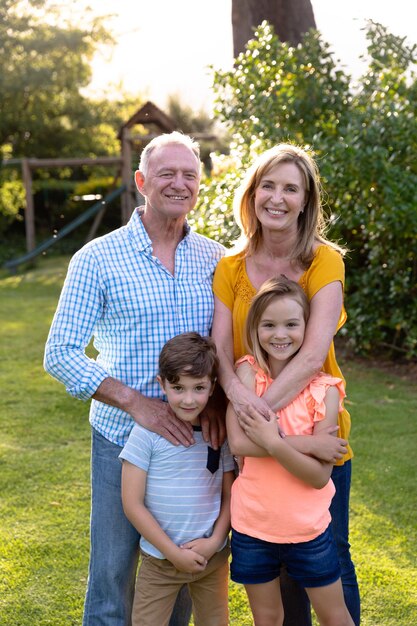 Portrait de groupe d'un couple caucasien et de leur petit-fils et petite-fille debout ensemble dans le jardin de leur maison, souriant à la caméra et embrassant