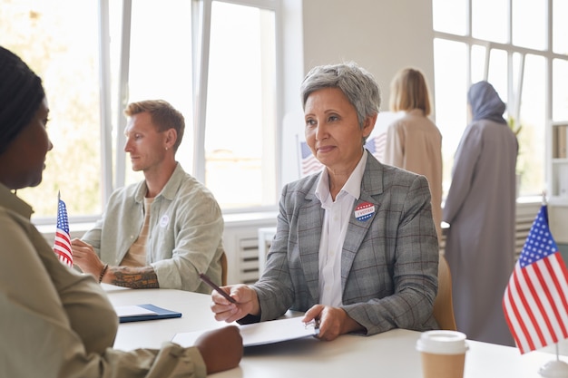 Portrait de groupe multiethnique de personnes votant au bureau de vote décoré de drapeaux américains, copy space