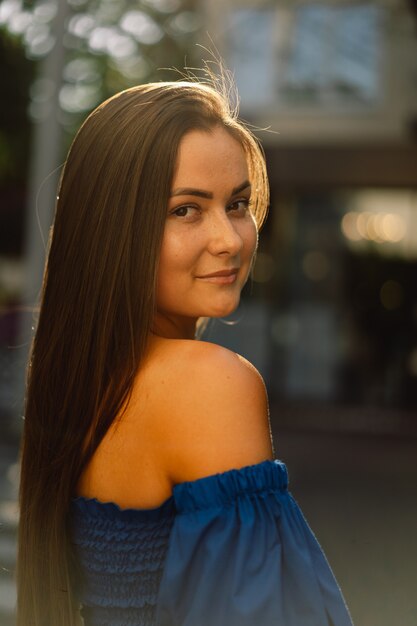 Portrait happy young woman wearing blue dress laughing looking at camera standing on street