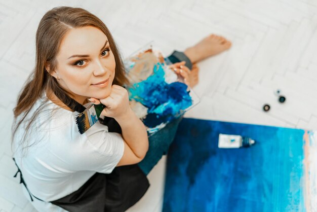 Portrait en haut angle d'une femme souriante avec une peinture assise sur le sol