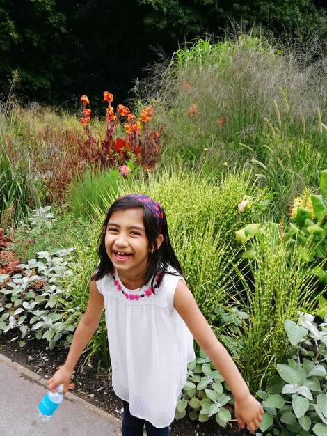 Portrait à haut angle d'une fille joyeuse debout contre des plantes dans un parc