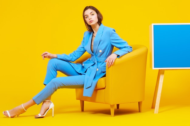 Portrait haute couture de jeune femme élégante en costume bleu. Fond jaune, tourné en studio