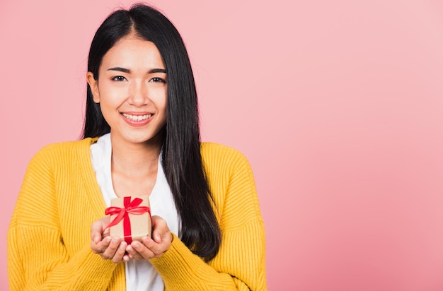 Portrait de l'heureuse belle jeune femme asiatique souriante tenant une petite boîte-cadeau sur les mains, prise de vue en studio isolée sur fond rose, anniversaire, nouvel an, Noël, Saint-Valentin, concept de jour férié