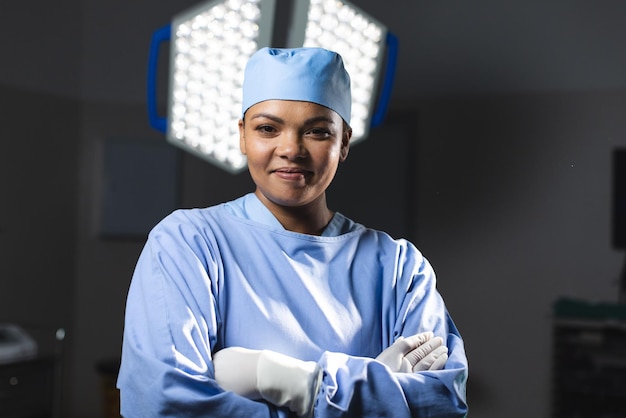 Portrait d'une heureuse chirurgienne biraciale portant une robe chirurgicale en salle d'opération