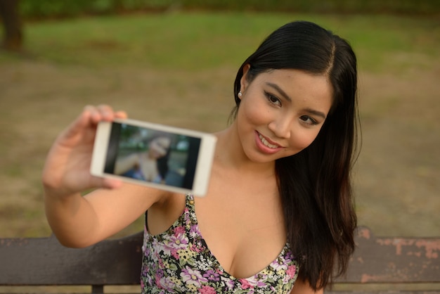 Portrait de l'heureuse jeune belle femme asiatique prenant selfie dans le parc