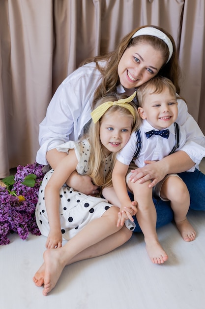 Portrait heureuse jeune femme européenne assise sur le sol avec son fils et sa fille et les étreignant