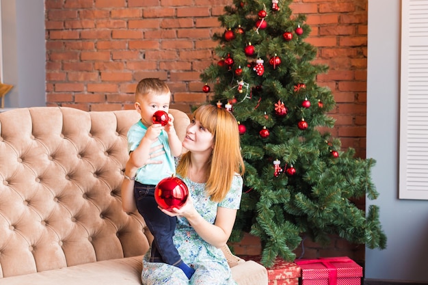 Portrait de l'heureuse mère et bébé qui rit tenant la boule contre l'intérieur festif domestique avec