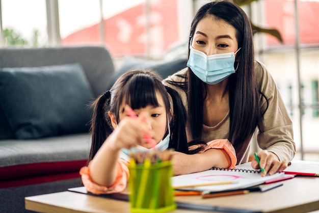 Photo portrait heureux amour mère de famille asiatique enseigner à la petite fille fille asiatique apprendre et étudier sur tablemaman et jeune fille asiatique écrivant avec un livre et un crayon faisant ses devoirs à l'école à la maison