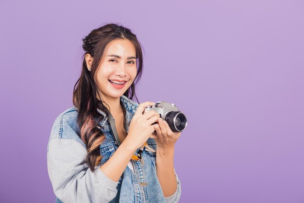 Portrait heureux asiatique belle jeune femme souriante excitée porter des denims tenant un appareil photo vintage, adolescente voyageuse photographe, prise de vue en studio isolée sur fond violet