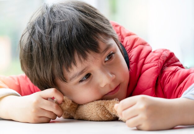 Portrait heureux enfant garçon jouant avec ours en peluche pose sur table