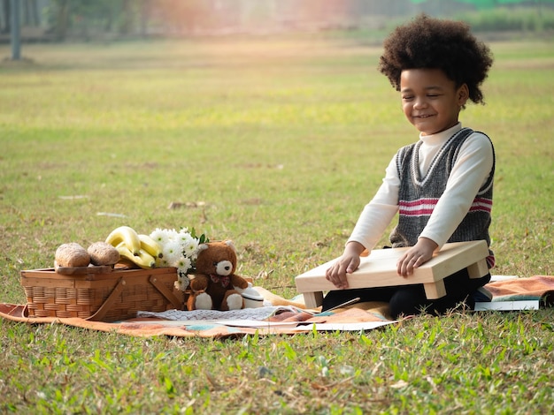 Portrait de l'heureux garçon afro-américain mettant une table de pique-nique dans le jardin le beau matinxAxA