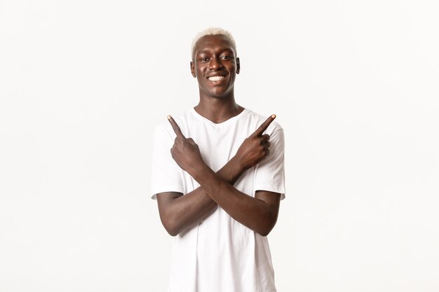 Portrait d'heureux homme blond afro-américain souriant, pointant du doigt sur le côté, montrant deux variantes