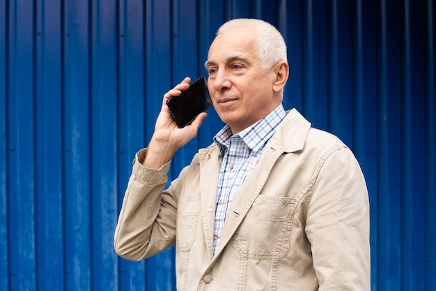 Portrait d'heureux homme mûr parlant avec smartphone en fond bleu, fond. Homme senior, technologie moderne