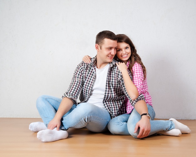 Portrait de l&#39;heureux jeune couple assis sur le sol, levant les yeux, prêt pour votre texte ou votre produit