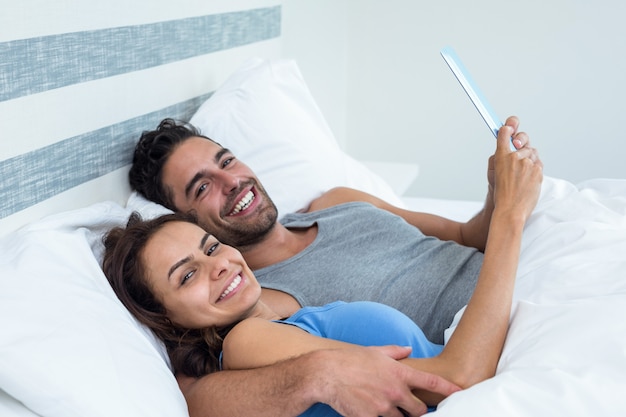 Portrait d'heureux jeune couple avec tablette en position couchée sur le lit